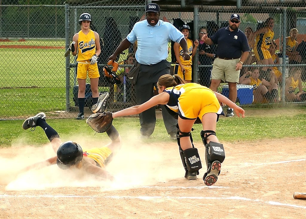 Youth softball player slides into home plate as the catcher attempts to tag. Sports action captured vividly.