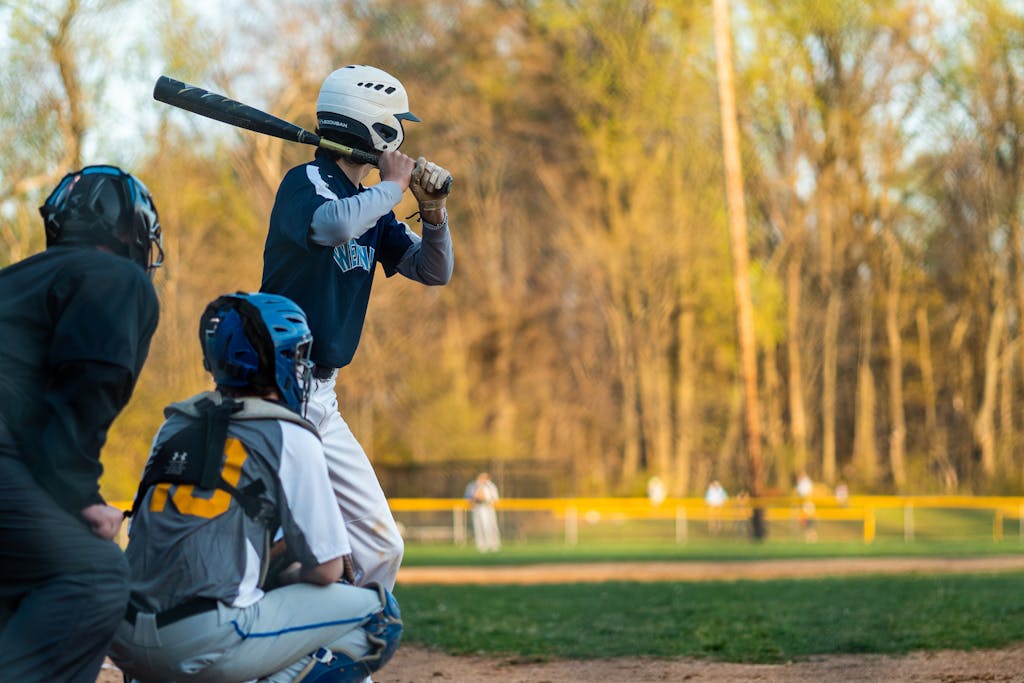 Baseball player in action at the plate during an outdoor game in a sunny park.