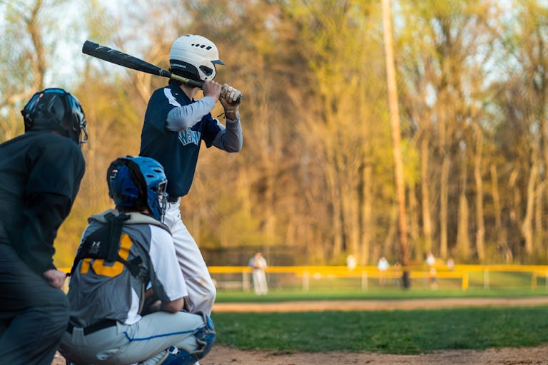 Baseball player in action at the plate during an outdoor game in a sunny park.